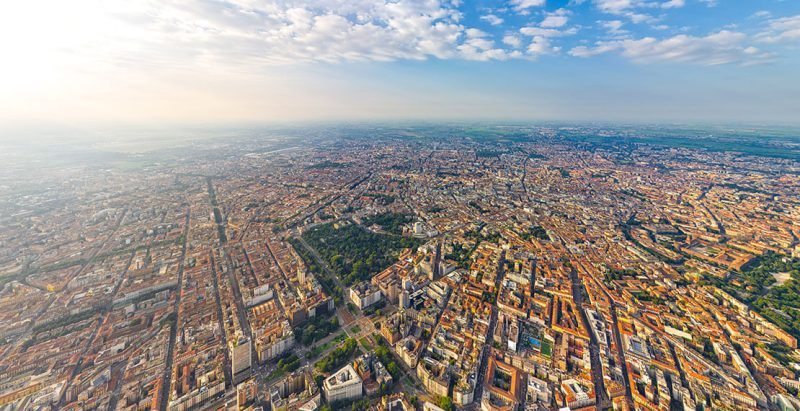Vista aerea di una città con edifici e spazi verdi sotto un cielo nuvoloso.