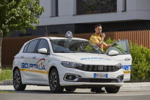 Auto Fiat bianca con logo 'SICURITALIA', persona con maglia gialla accanto alla portiera aperta