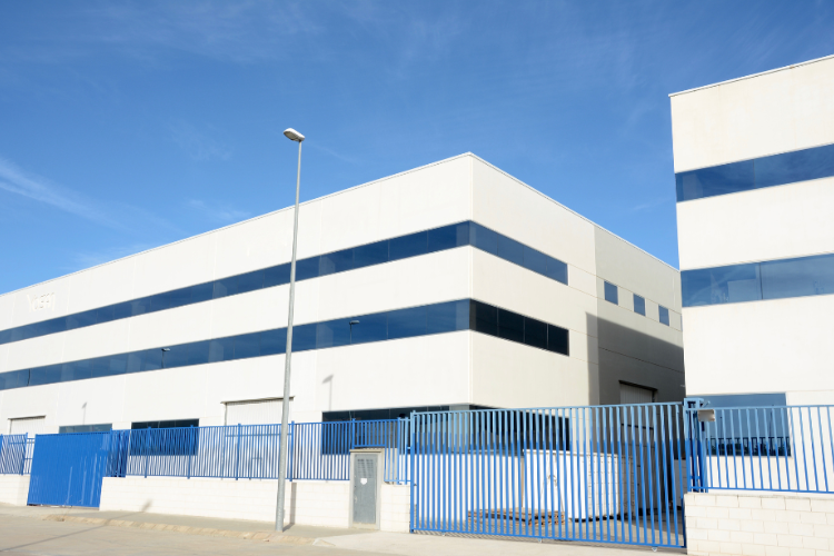 Edificio industriale bianco con strisce blu e recinzione, sotto un cielo sereno