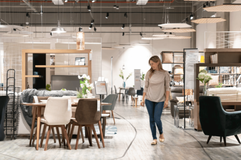 Interno di negozio di arredamento con persona tra tavoli e sedie.
