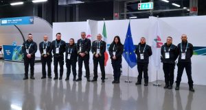 Operatori della sicurezza Sicuritalia schierati davanti alle bandiere e all’area del Media Center dei Giochi Milano Cortina 2026.